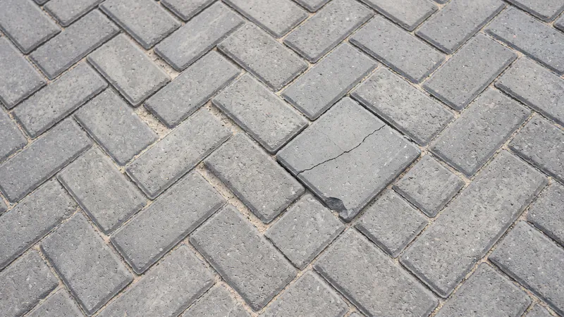 Close-up of grey herringbone block paving with one laid paver cracked across its face and chipped at one corner